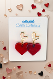 Red heart-shaped earrings with gold accents on a Colette Collections card, surrounded by decorative hearts.