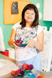 adult with disability holding a fused glass bowl hand made in shades of pink, peach, purple and light blue