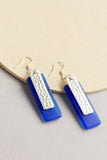 angle view of Telina rectangular drop earrings in blue with a sea glass texture and silver hammered rectangular accent layered on top handmade by people with disabilities
