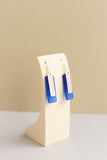hanging view of Telina rectangular drop earrings in blue with a sea glass texture and silver hammered rectangular accent layered on top handmade by people with disabilities
